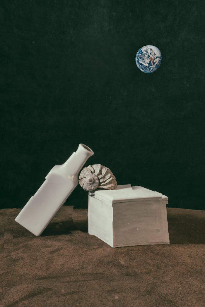 Surreal composition of a ceramic bottle and box on a textured surface with Earth in the background.